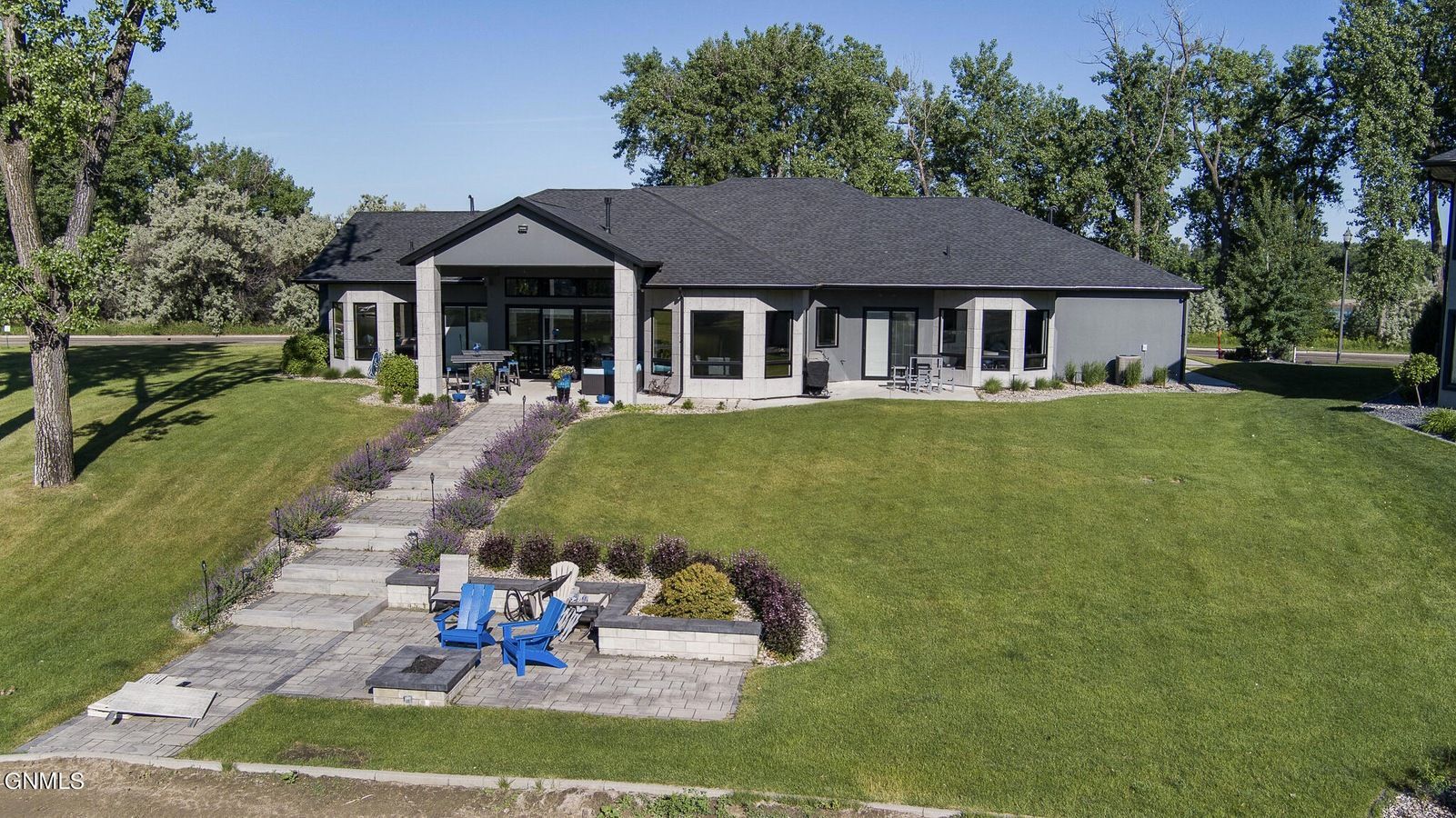 An aerial view of a dark gray house with a stone walkway leading to a stone patio with blue chairs and a fire pit.