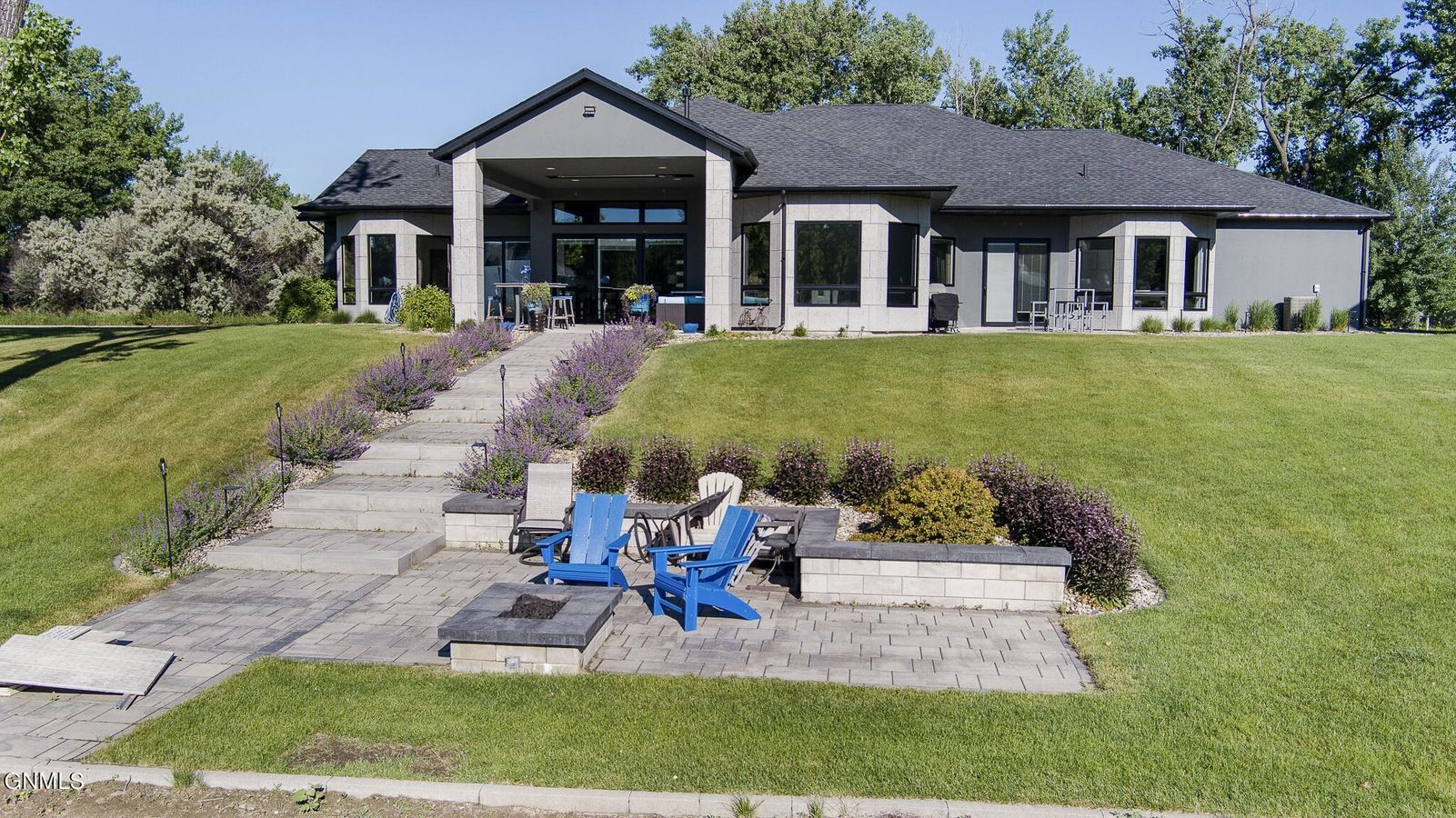 A modern gray house with a stone patio, fire pit, two blue chairs, and a long set of stairs leading to the front entry.