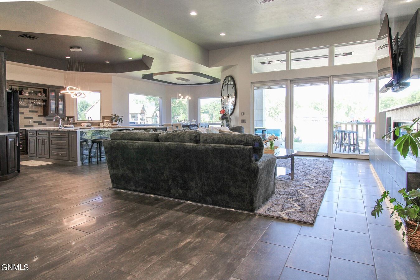 An open-concept living area with dark wood floors, a plush sofa, a kitchen island, and large windows leading to a patio.