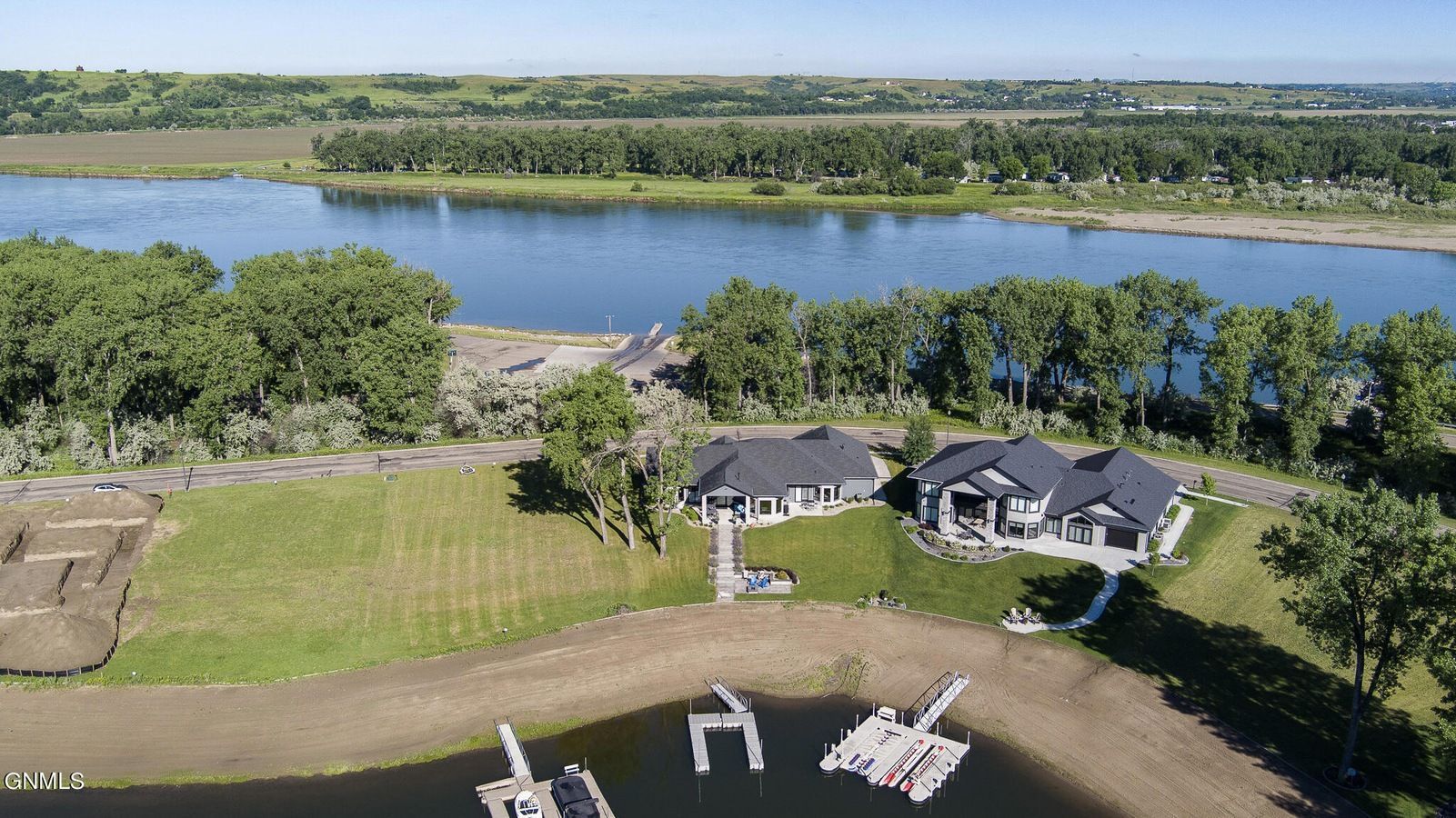 An aerial view of a luxury house with a boat dock on a pond, nestled near a river and lush green landscape.