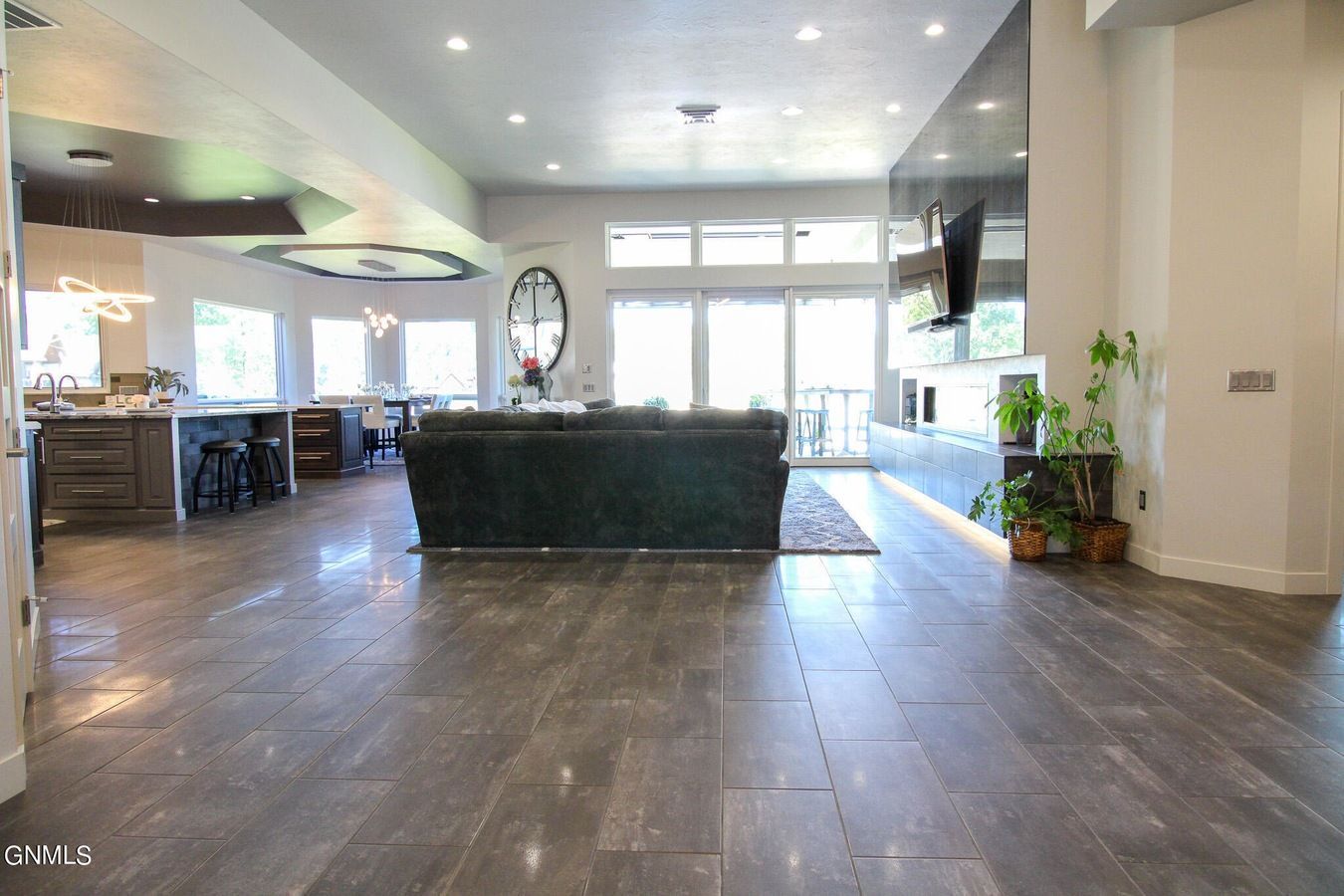 A spacious, open-concept living area with dark tile flooring, a large black sofa, and a modern fireplace wall.