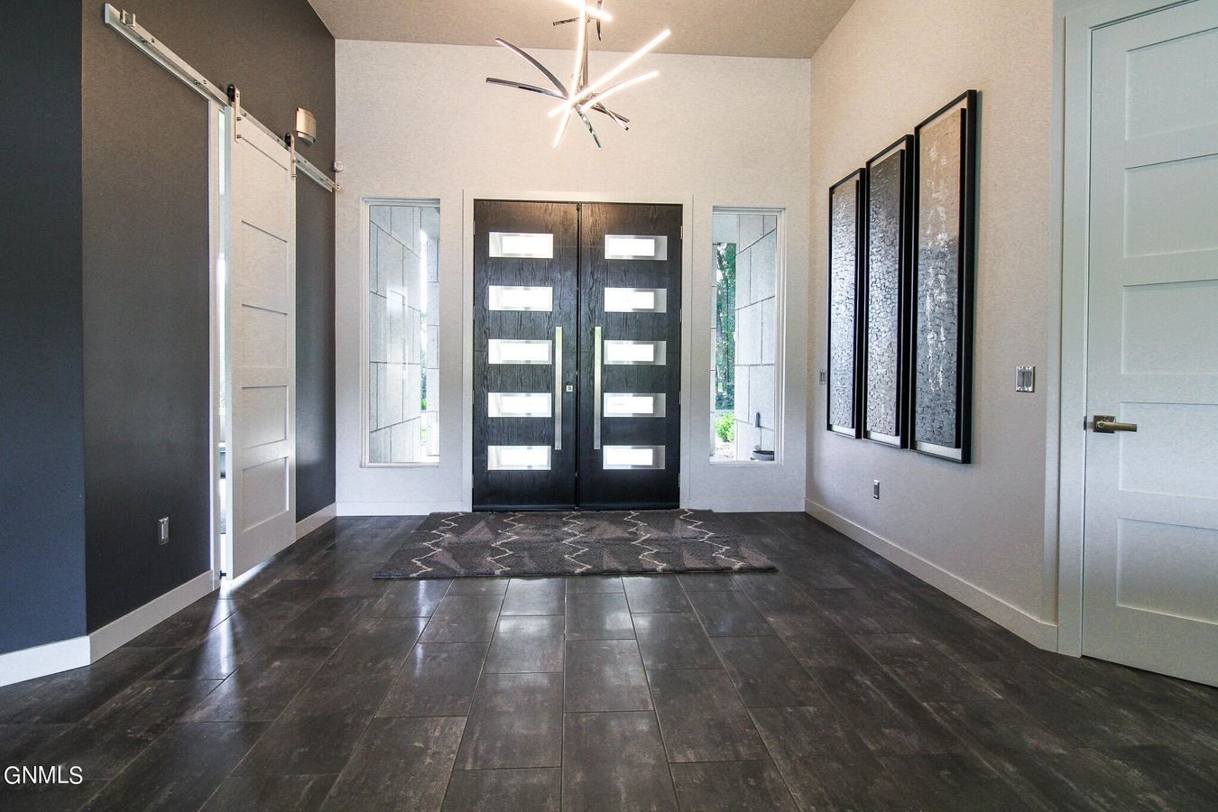 A bright, modern entryway with dark wood floors, double doors, side windows, a sputnik chandelier, and wall art.