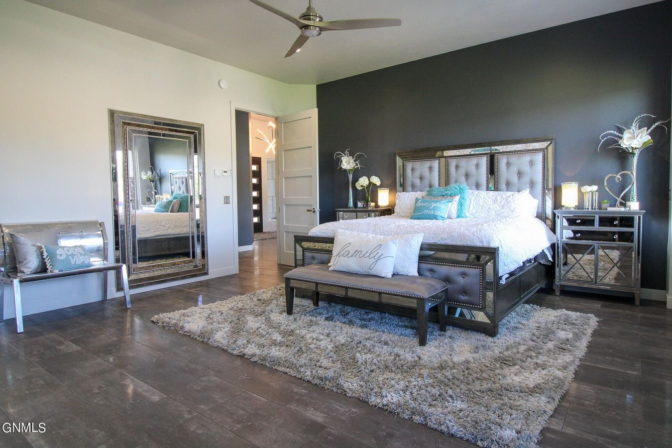A luxury bedroom with a king-sized bed, dark accent wall, mirrored furniture, large floor mirror, and grey area rug.