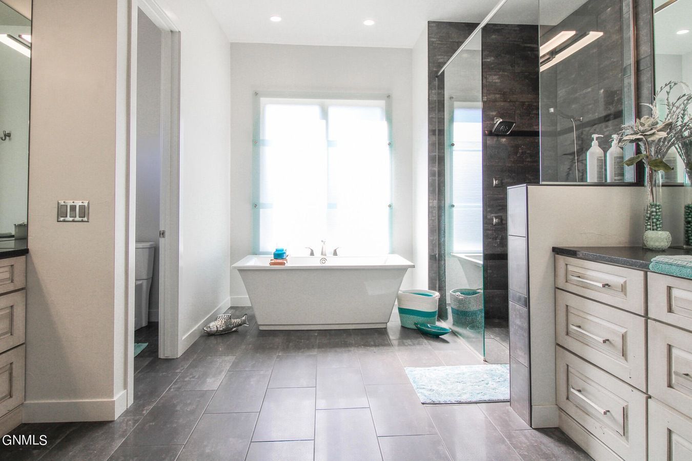 Modern bathroom with a white soaking tub, dark wood floors, gray tiled shower, and white vanity cabinets.