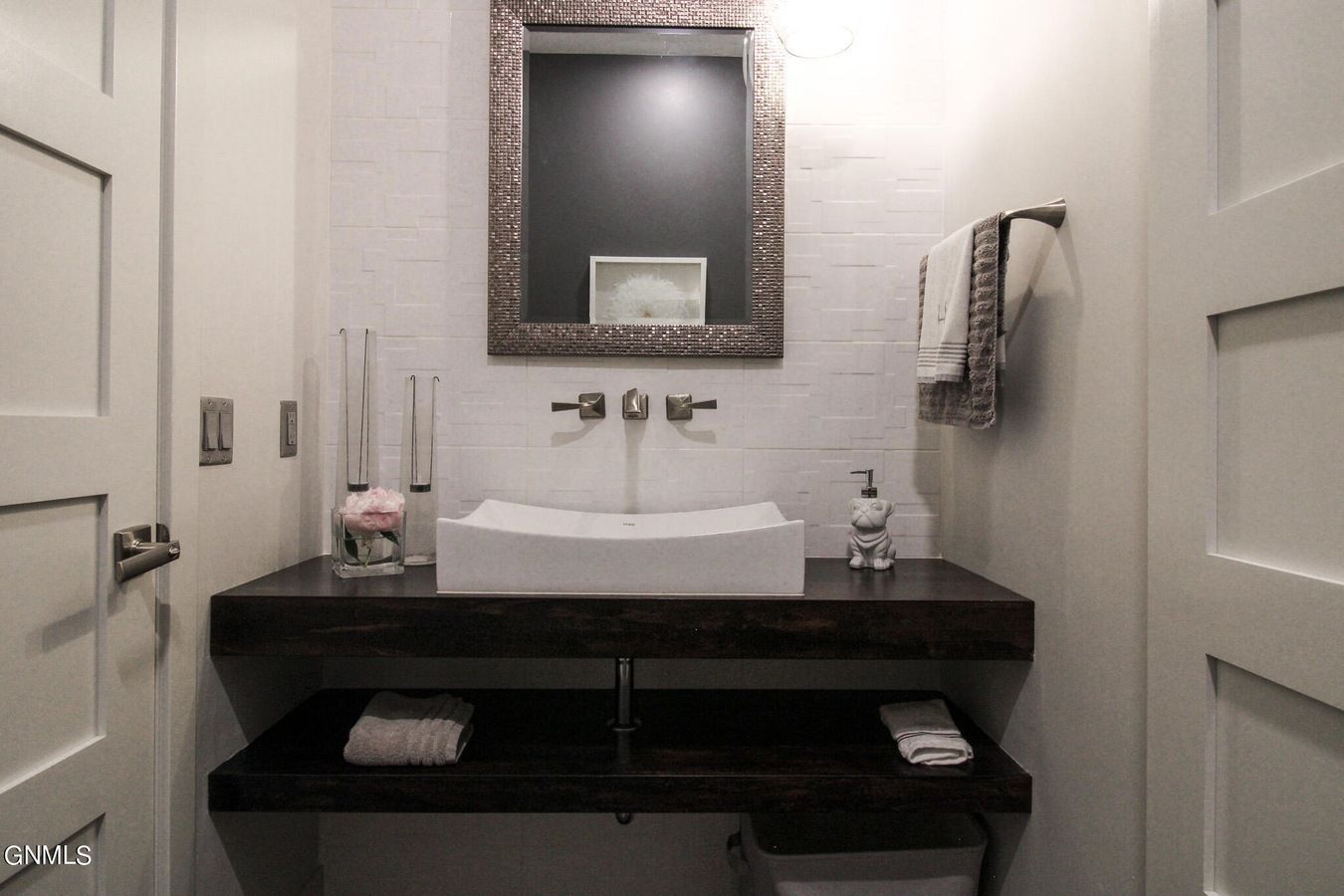A modern powder room with a white vessel sink on a dark wood shelf, a textured wall, and a framed mirror above.