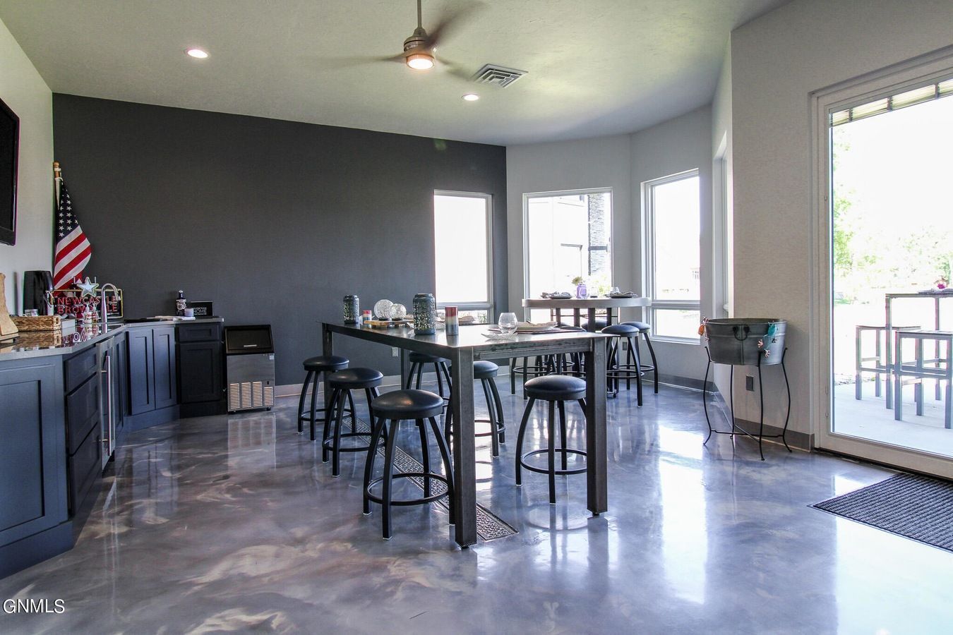 A modern kitchen and dining space with dark gray cabinets, a long table, high bar stools, and shiny marbled gray floors.