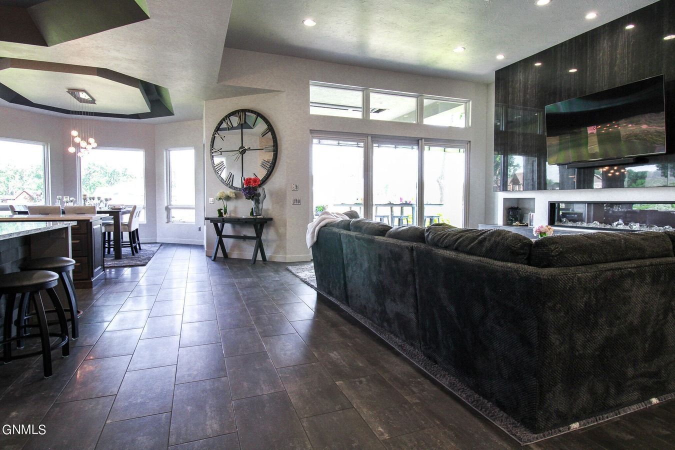 An open-concept living area with a large gray sectional, a fireplace with a TV, tiled floors, and an adjacent dining area.