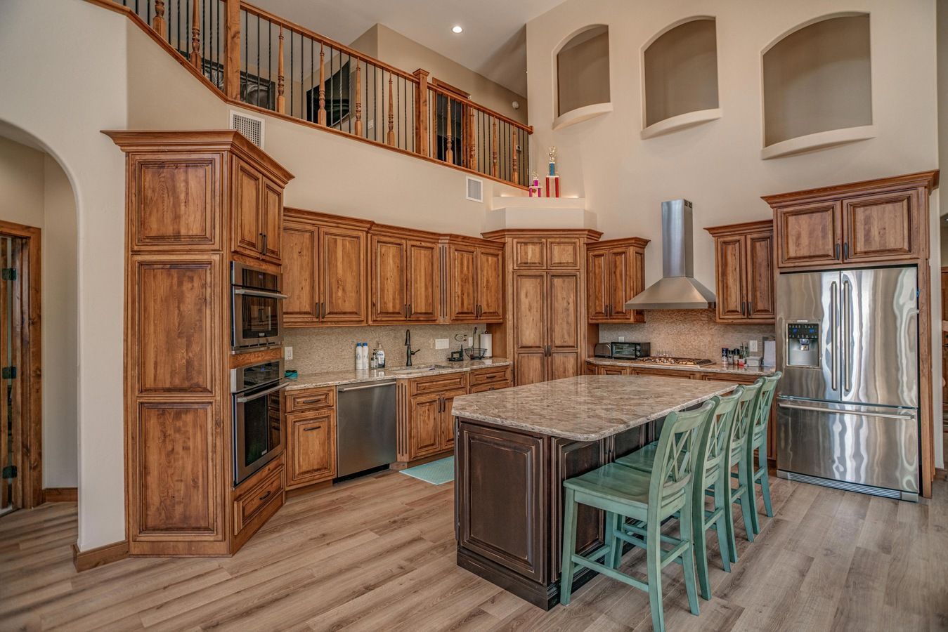 Spacious kitchen with wood cabinets, granite countertops, a central island with teal stools, and high vaulted ceilings.