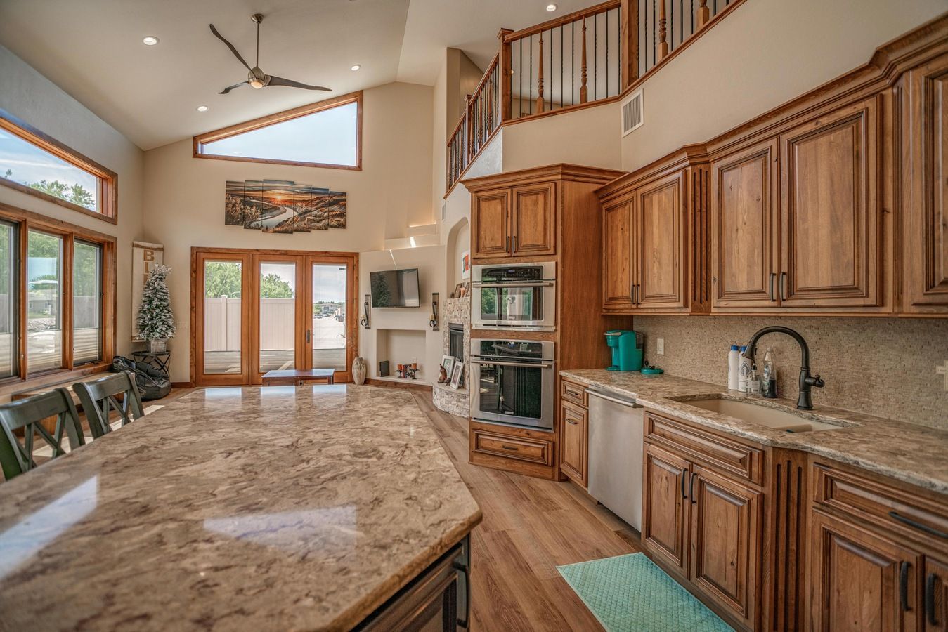 A spacious kitchen featuring honey-toned wood cabinets, granite countertops, a large island, and high ceilings with windows.