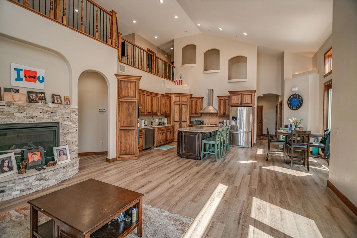 Open-concept living room and kitchen featuring wooden cabinetry, stone fireplace, island seating, and hardwood floors.