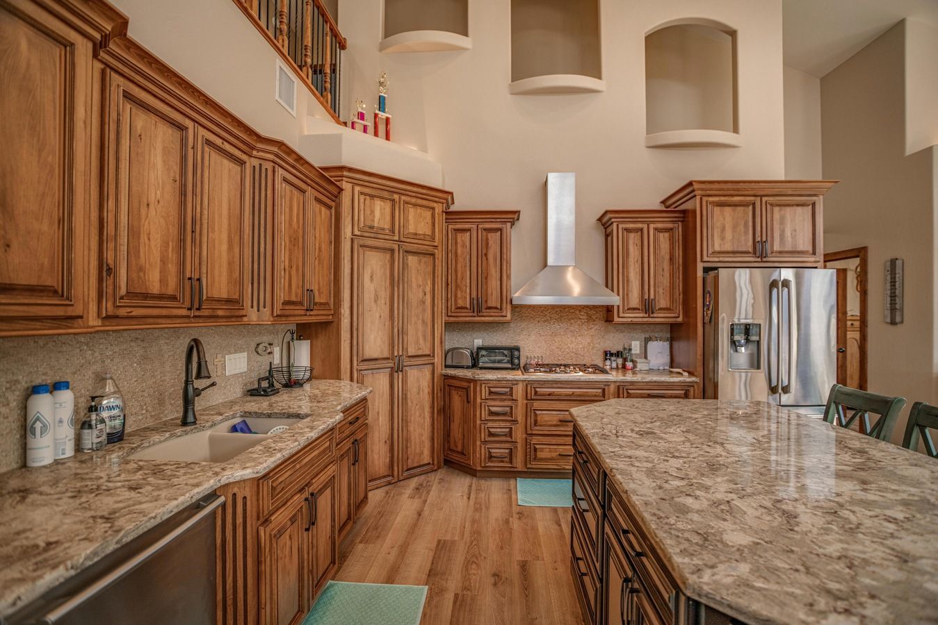 Modern kitchen with wood cabinets, stainless steel appliances, and a large granite island under high ceilings.