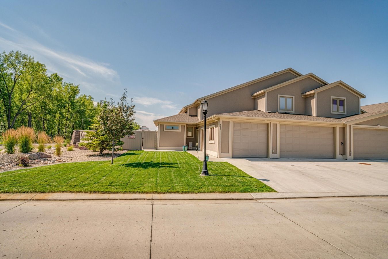 A beige multi-unit house with garage doors, a green lawn, and a sidewalk under a clear blue sky.
