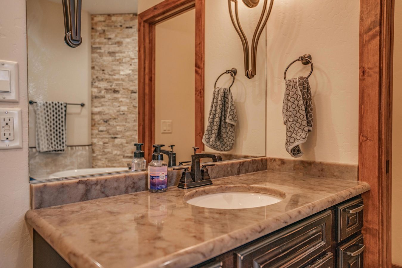A bathroom vanity with a marbled stone countertop, dark wooden cabinets, a sink, and two hanging patterned hand towels.