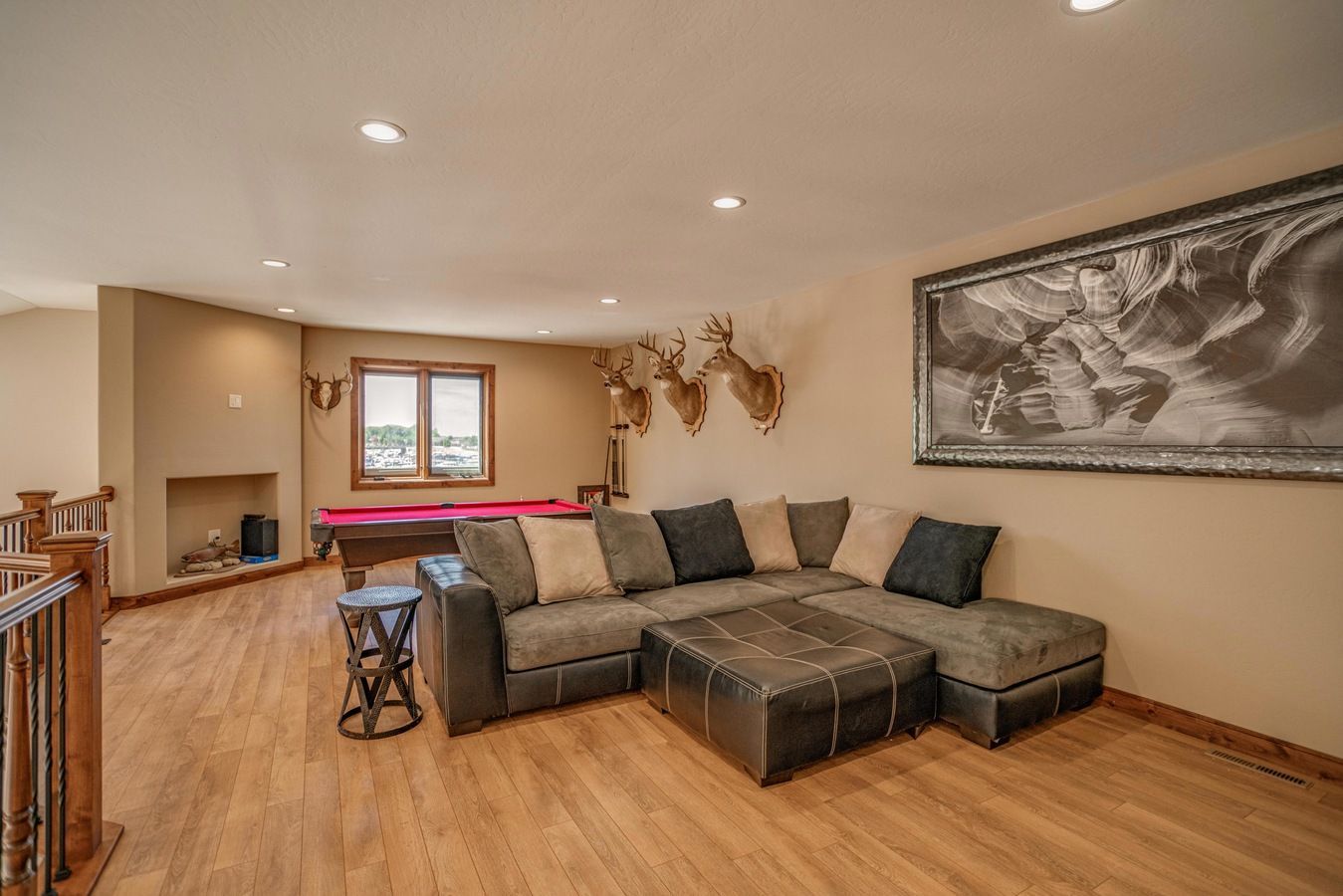 A game room with a grey sectional, a large black-and-white framed print, taxidermy deer heads, and a red pool table.