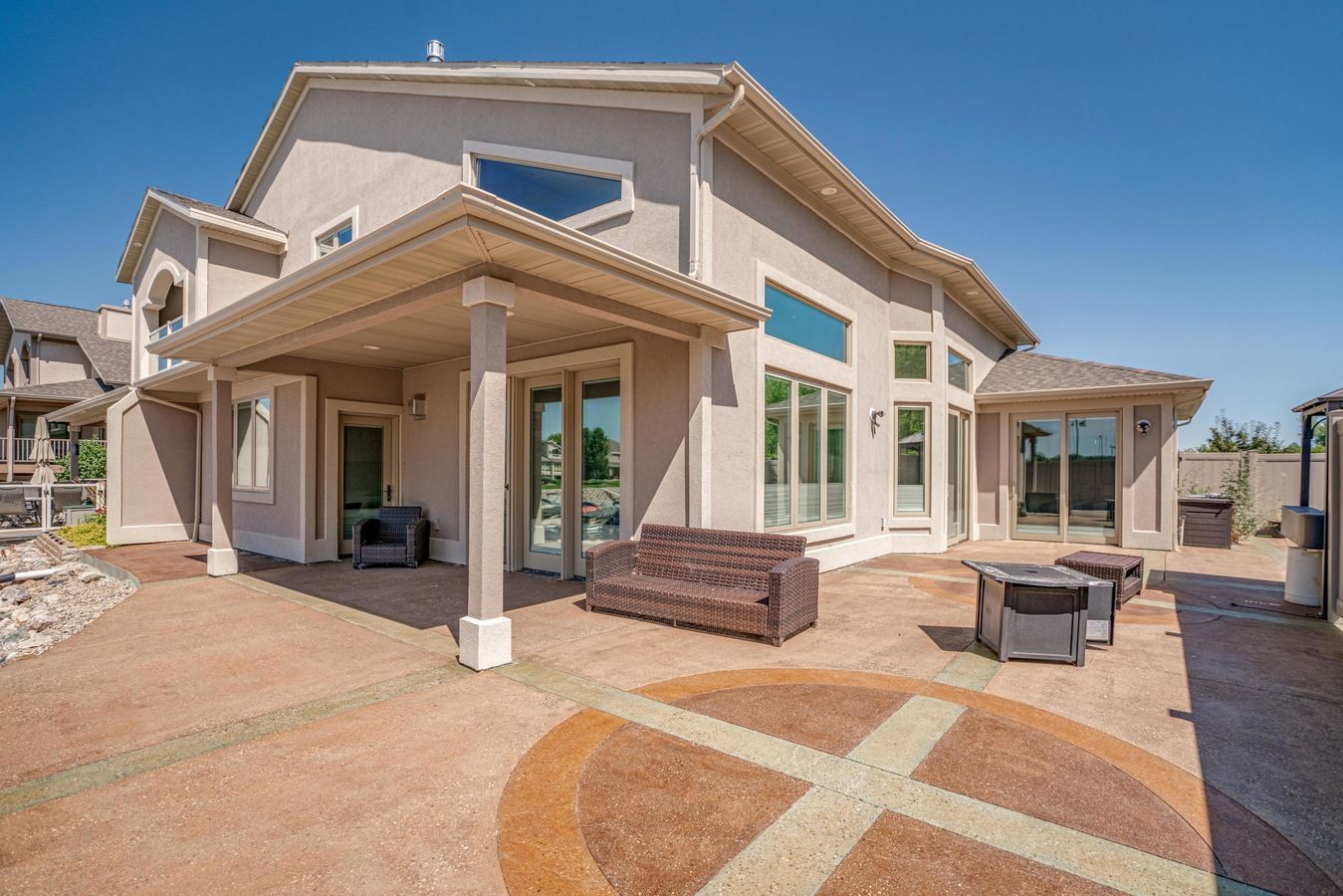 Tan house with a covered patio, outdoor seating, and a decorative concrete floor under a clear blue sky.