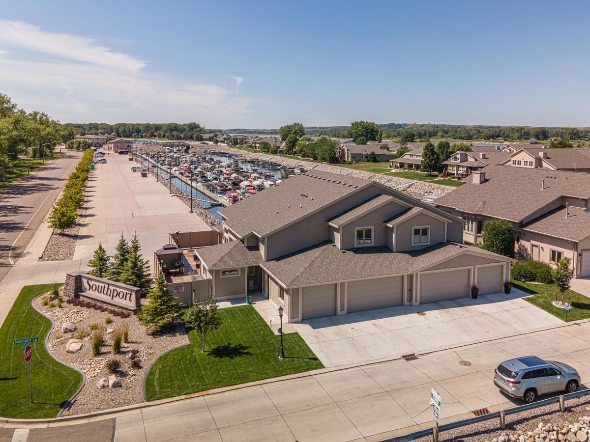An aerial view of a tan residential complex with a multi-car garage, near a marina and parking lot under a blue sky.