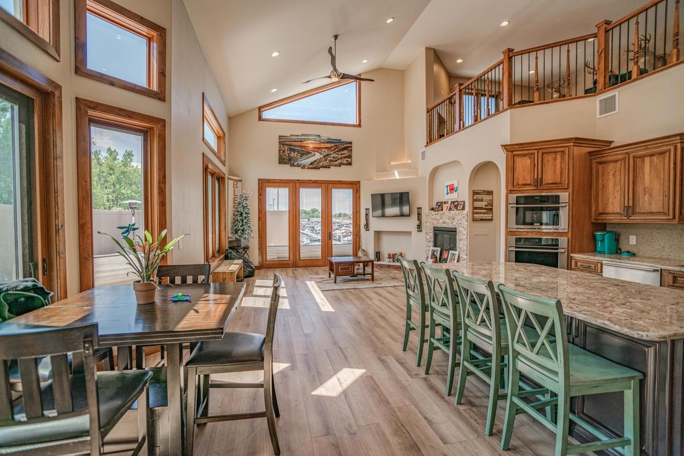 A bright, open-concept living area with a wooden dining table, a kitchen island with green chairs, and vaulted ceilings.