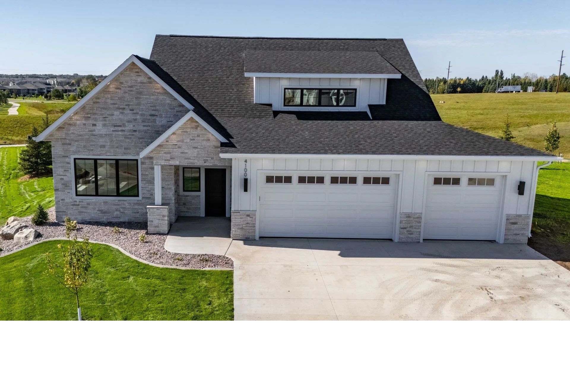 A modern house with a stone and white siding exterior, dark shingled roof, three-car garage, and a manicured front lawn.