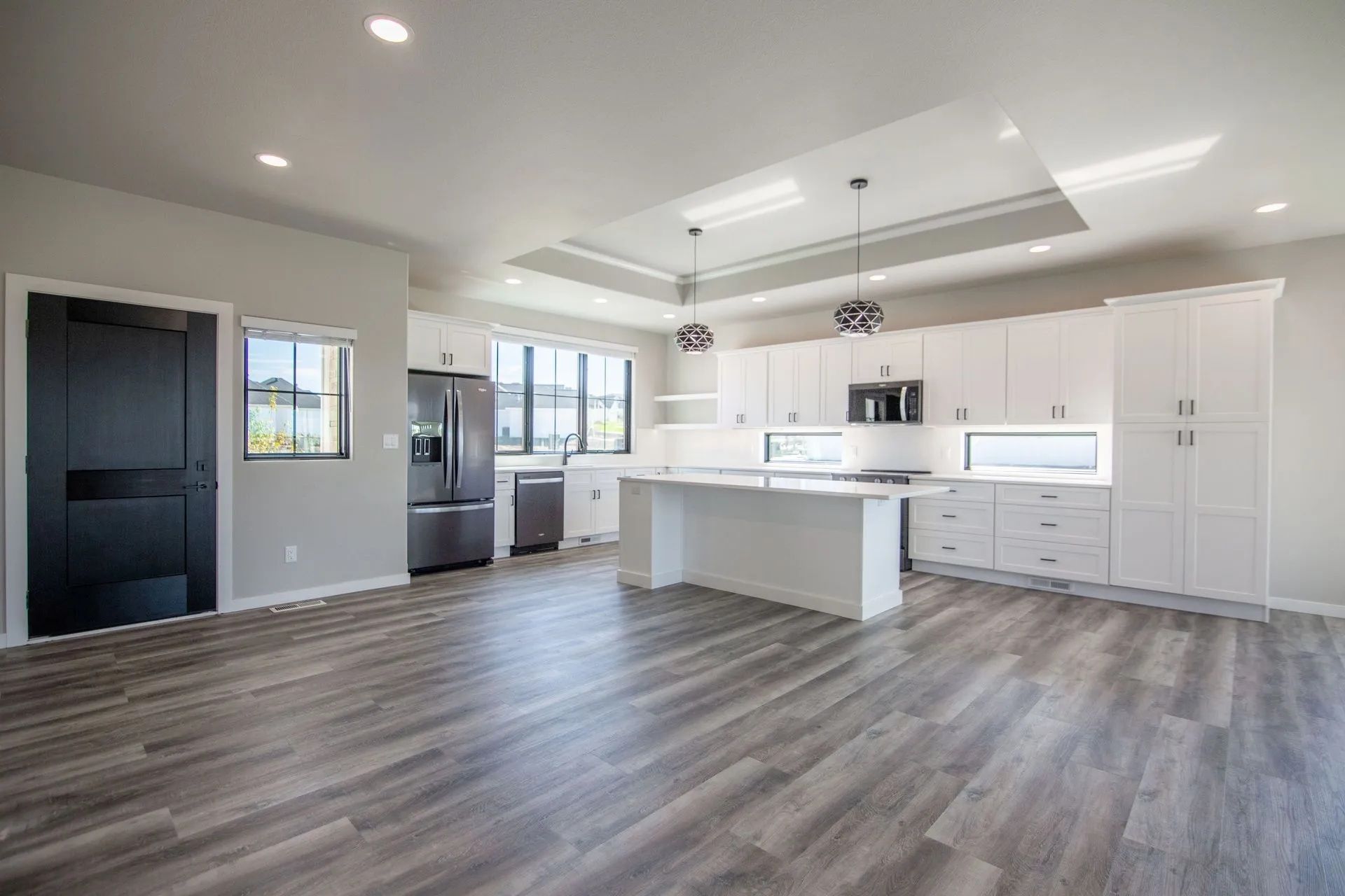 A modern, open-concept kitchen with white cabinetry, a central island, stainless appliances, and gray wood-look flooring.