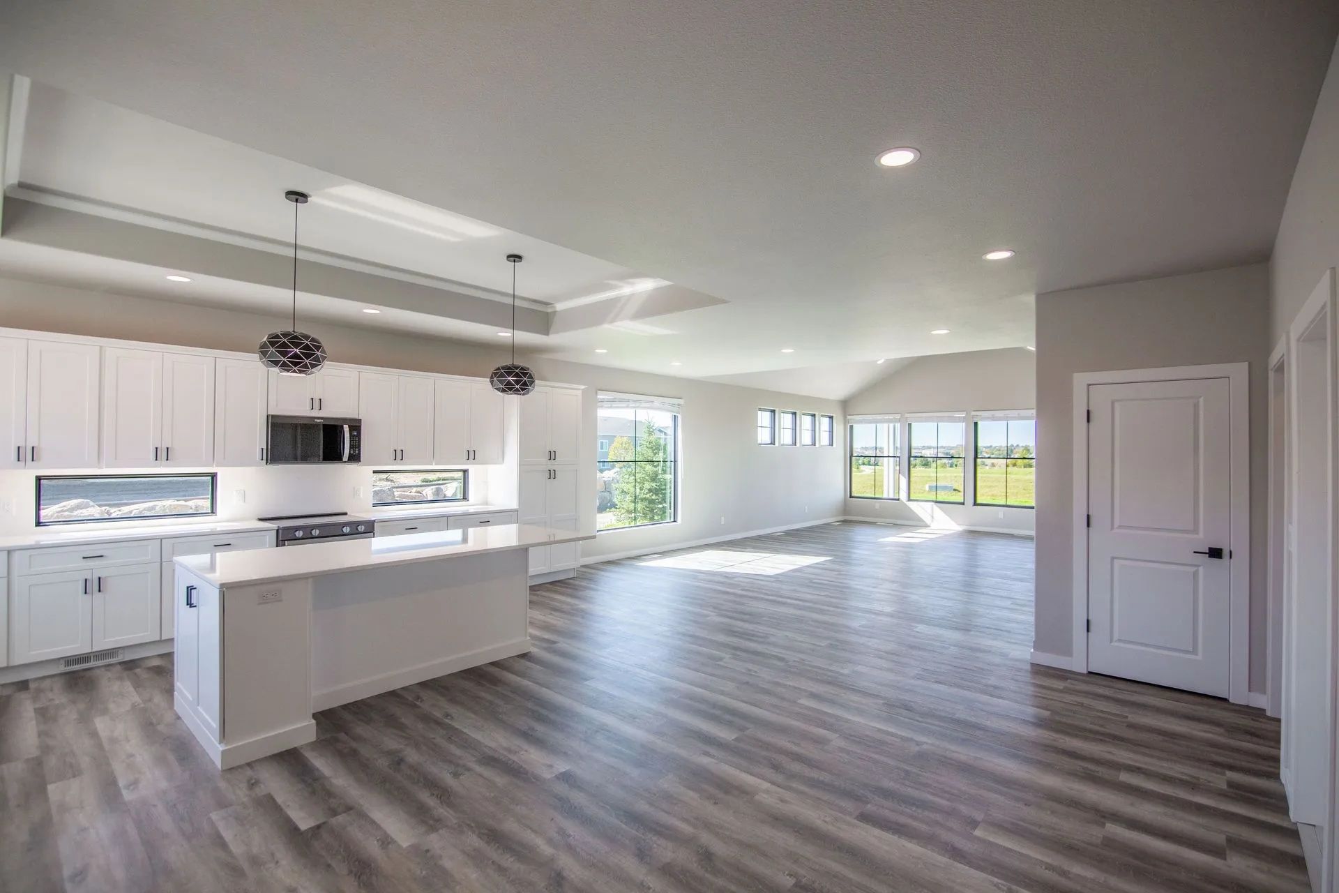 Modern, open-concept kitchen and living area featuring white cabinets, a kitchen island, and light-toned wood flooring.