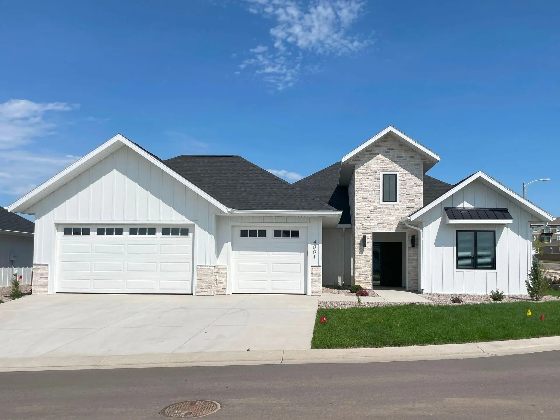A modern farmhouse with transitional elements, clean modern lines with classic warmth, Board and batten siding, Stone Entryway, Black Windows, Black Shingle Roof, 3-stall garage.
