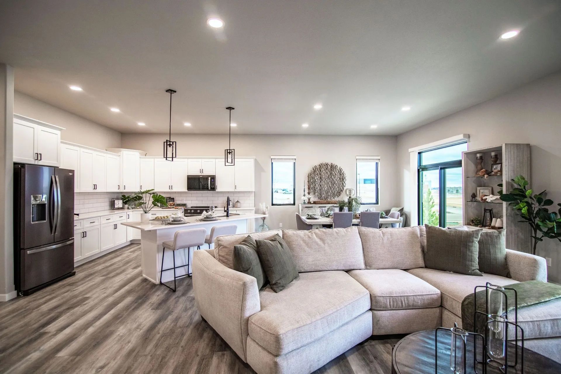 An open-concept living area with a modern kitchen, white cabinets, and a large beige sectional sofa on wood-look flooring.