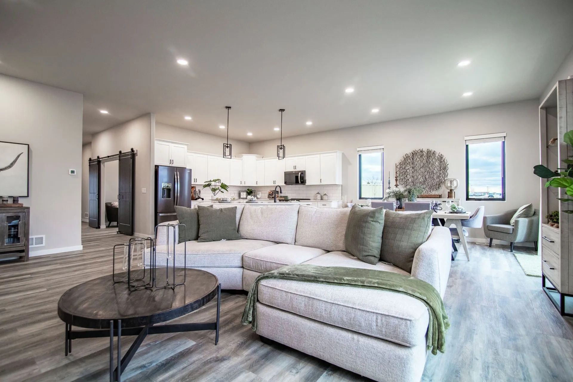 Open-plan living room with a cream sectional sofa, dark wood coffee table, and an adjacent white kitchen.