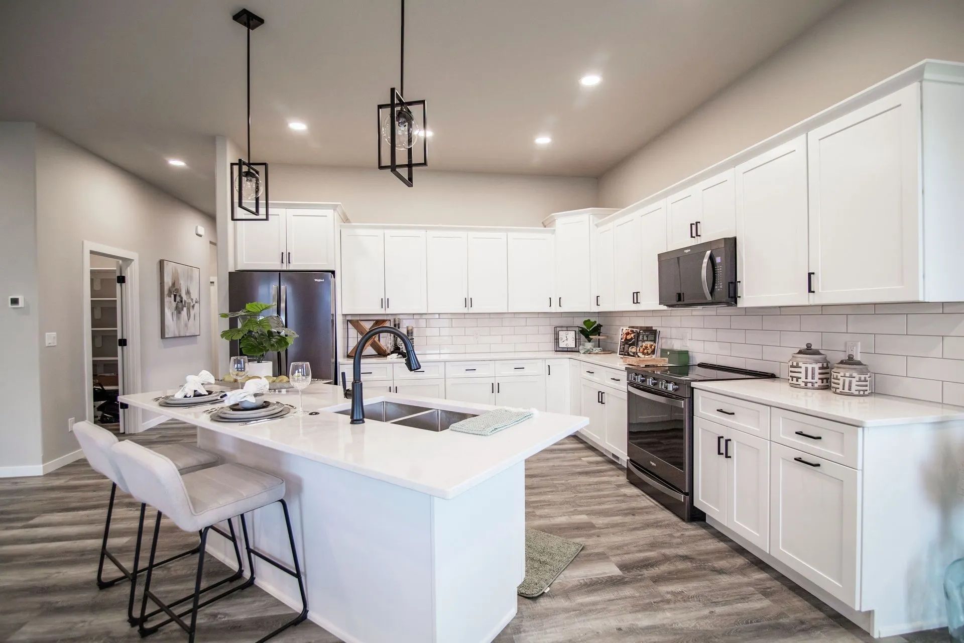 A bright, modern kitchen featuring white cabinets, a large island with two chairs, stainless appliances, and wood floors.