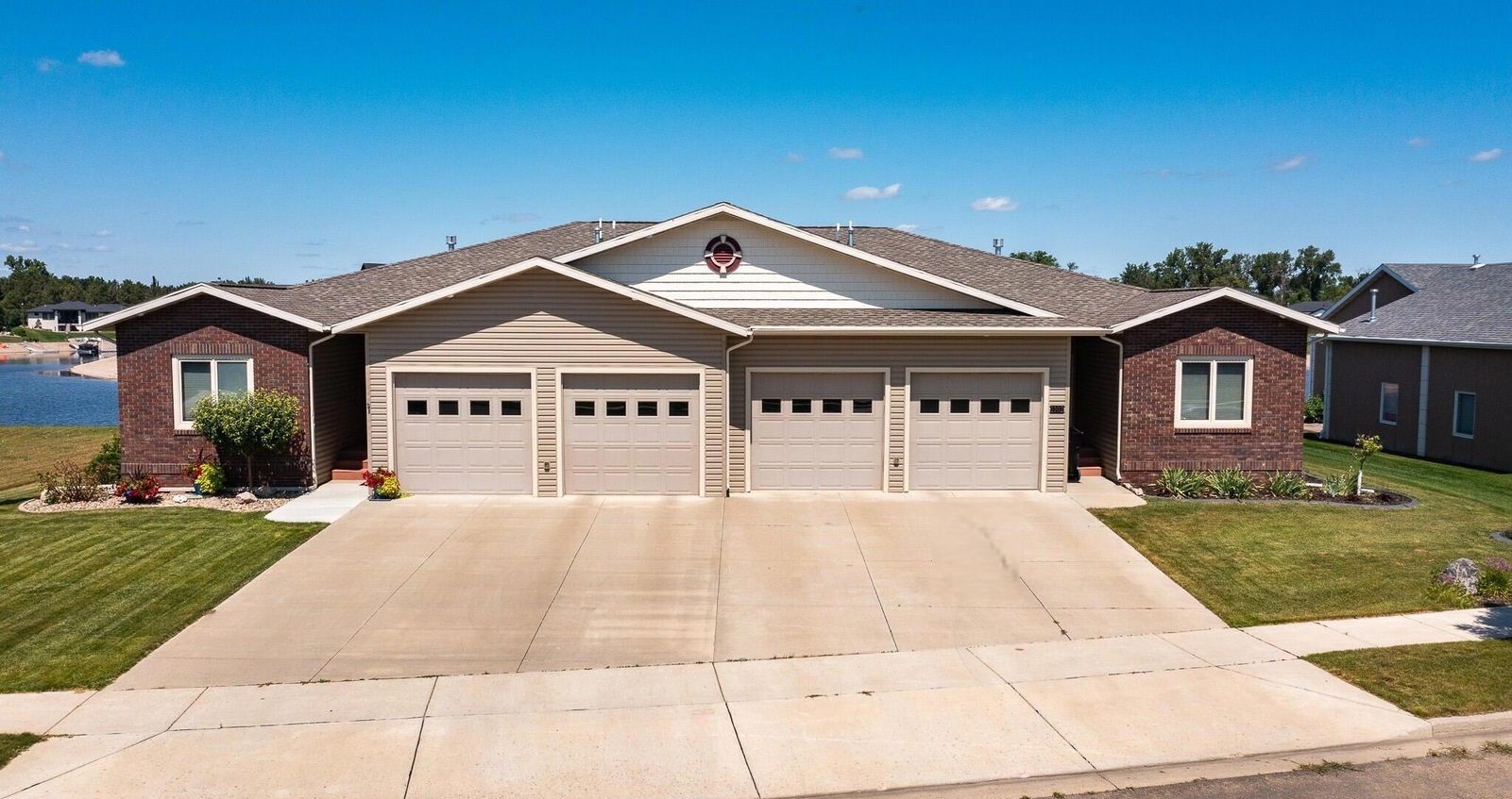 A tan duplex with brick siding, four garage doors, and a front lawn under a clear blue sky.