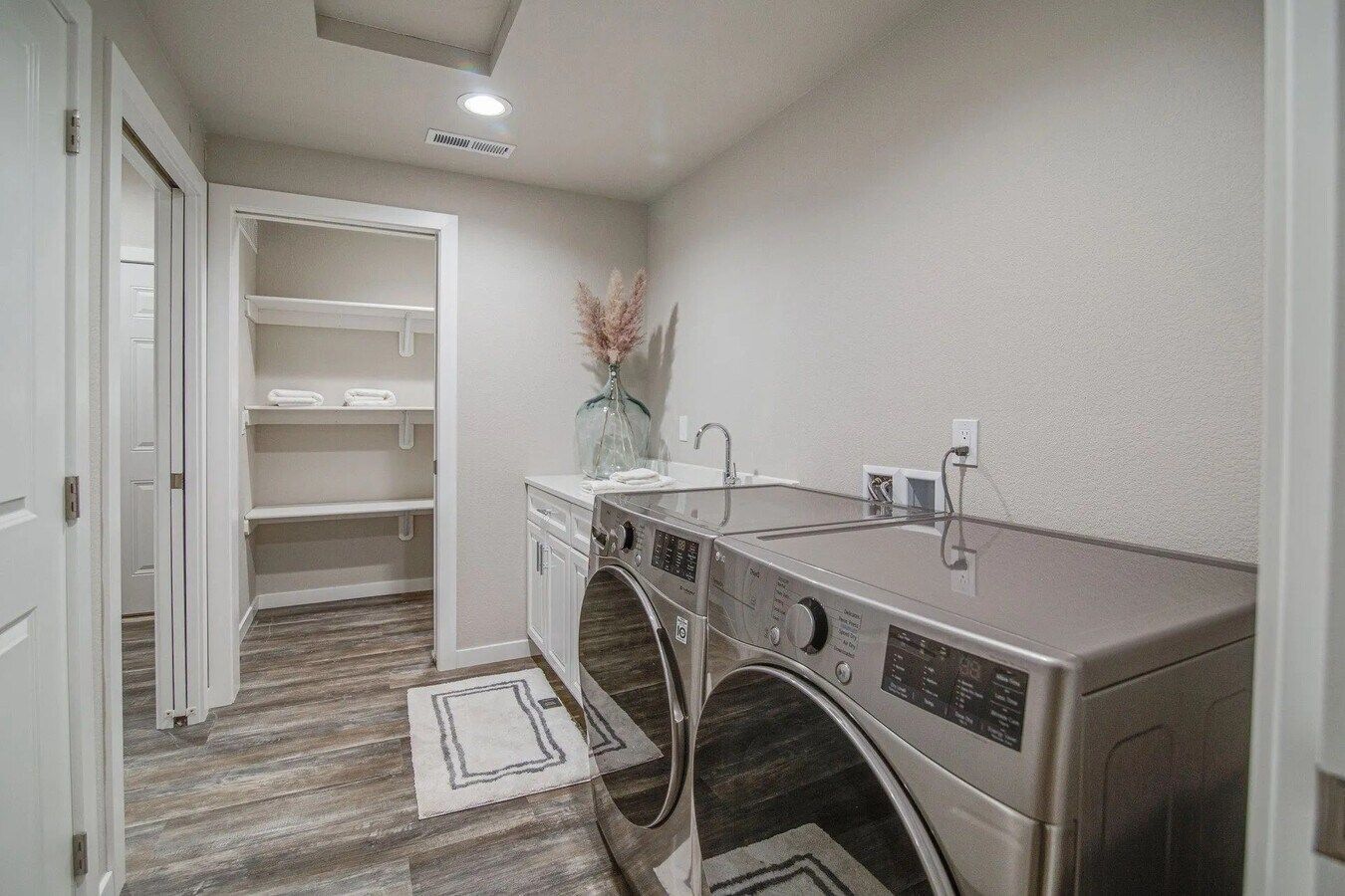 A laundry room with a front-load washer and dryer, a sink, a built-in pantry with shelves, and wood-look flooring.