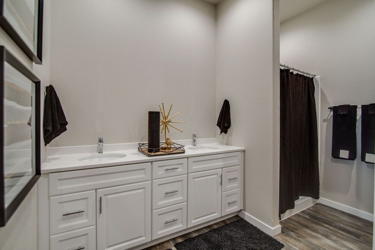 A modern bathroom with a double white vanity, granite countertop, neutral walls, and a dark shower curtain.