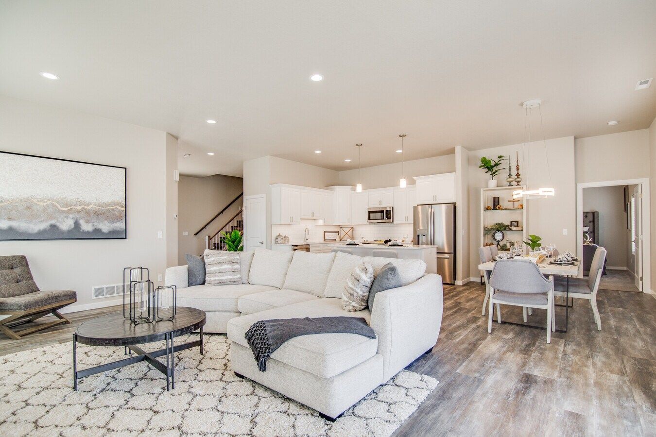A modern open-plan living room with a white sectional sofa, patterned rug, coffee table, and adjacent kitchen and dining.