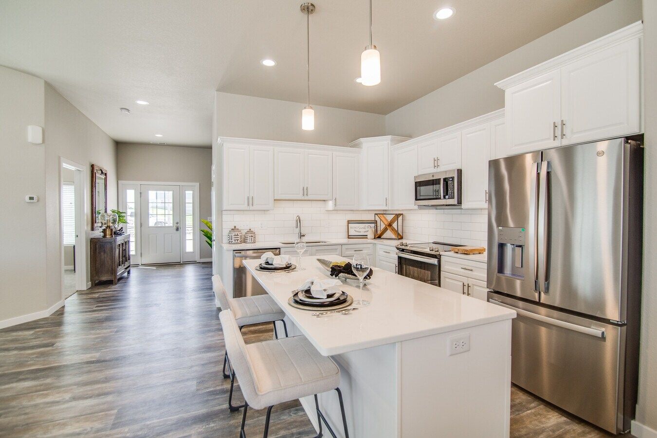 Modern kitchen with white cabinetry, stainless steel appliances, a white island with two stools, and wood-look flooring.