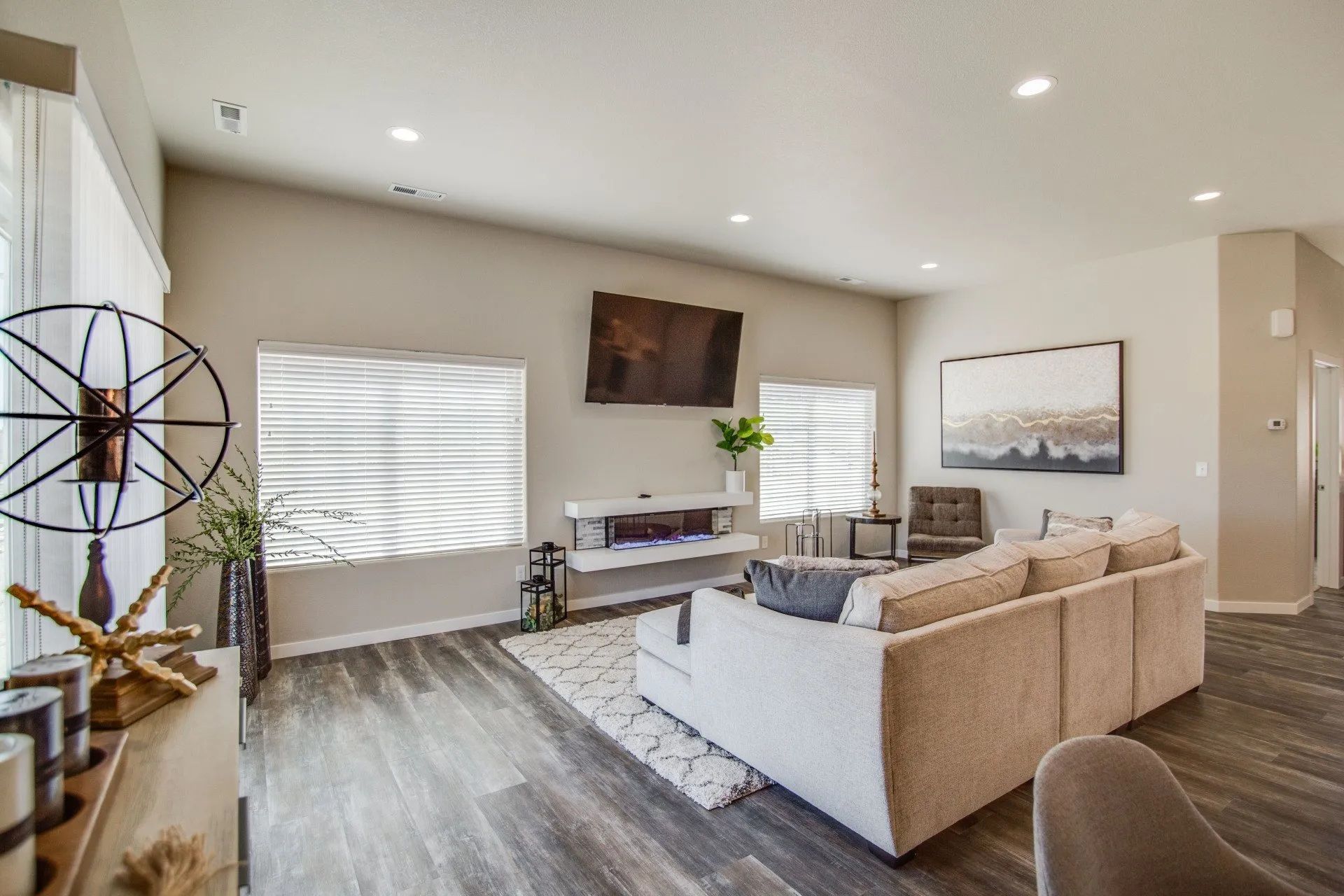 A modern living room with a neutral sectional sofa, a fireplace under a mounted TV, and wood-look floors.