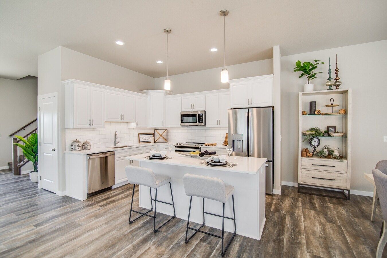A bright, modern kitchen with white cabinets, a central island with two chairs, stainless appliances, and wood-look floors.