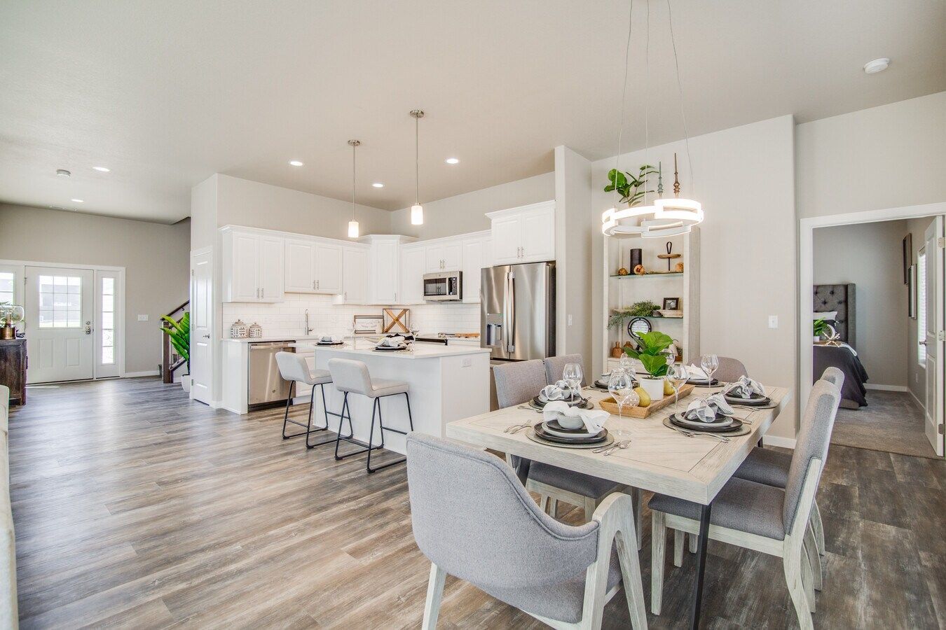 Modern open-concept kitchen and dining area with white cabinets, wood-look flooring, and a set dining table.