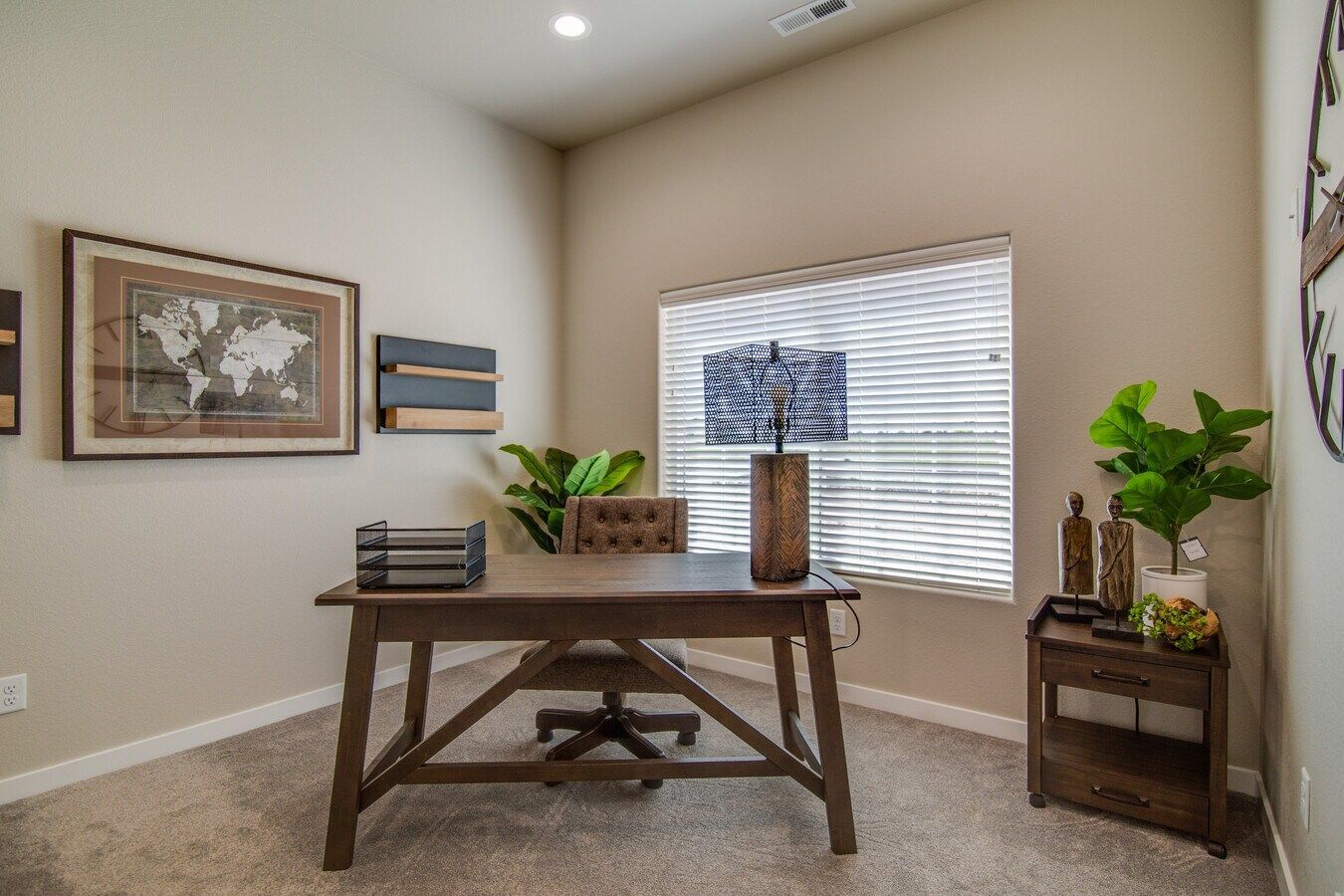 A home office featuring a wooden desk, an office chair, a world map wall art, a window with blinds, and a small side table.