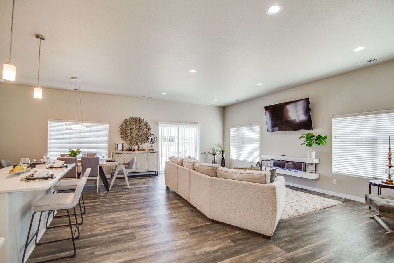 An open-concept living and dining room with a neutral sectional, a mounted TV, and wood floors.
