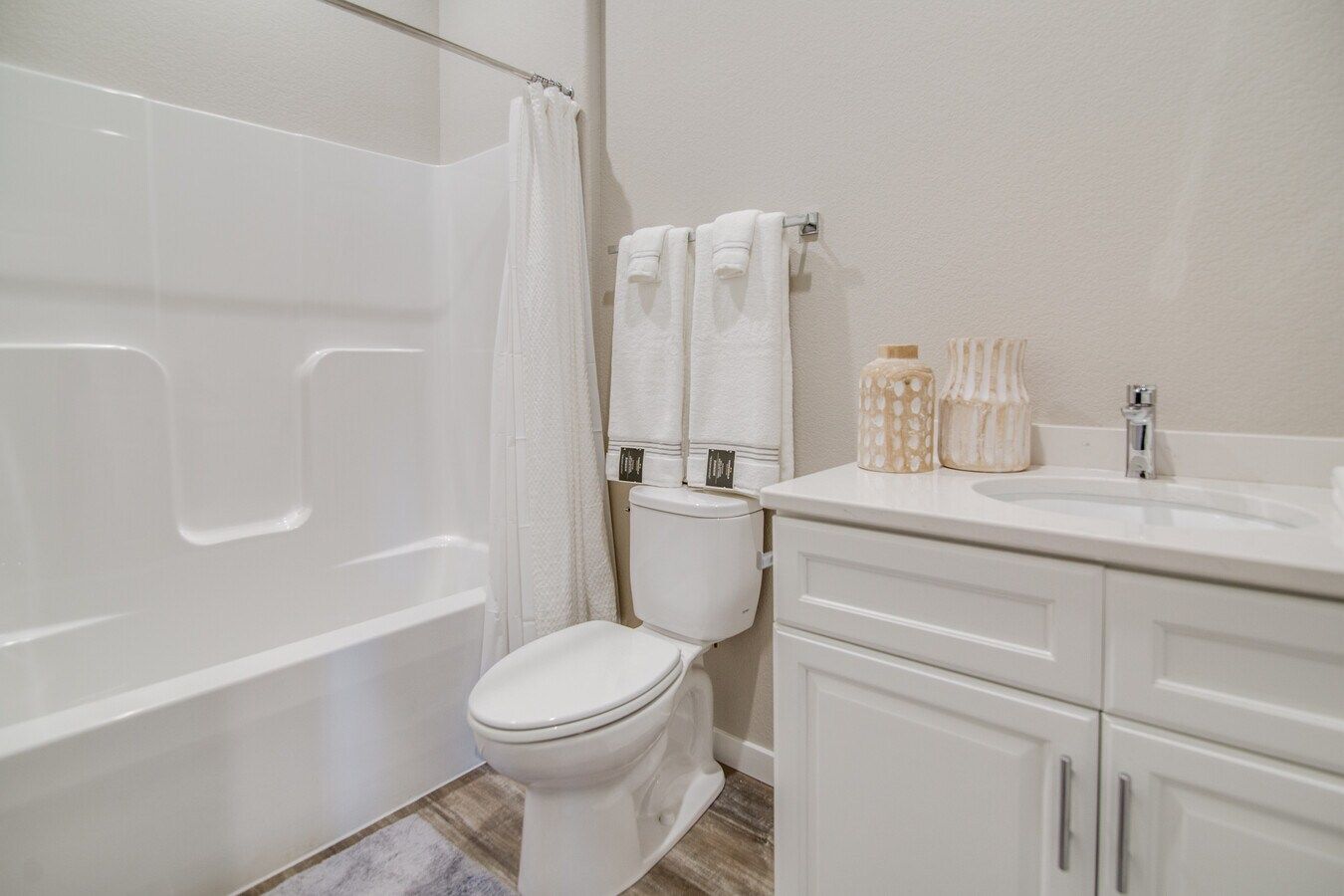 A clean, modern bathroom with a white shower-tub unit, a toilet with two white towels hanging above, and a white vanity.