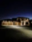 A long, low building illuminated by warm lights at night, set against a dark blue twilight sky.