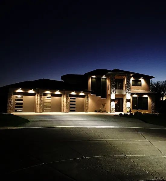 A multi-car garage home illuminated by exterior lights against a clear, dark evening sky.