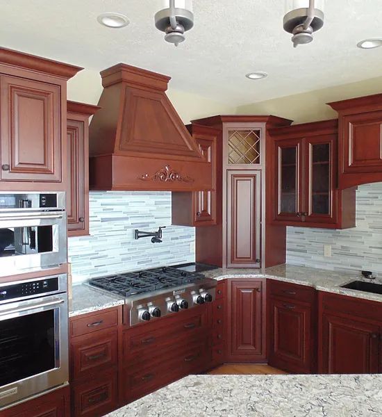 Kitchen with cherry wood cabinets, stainless steel appliances, a vent hood, and light-colored granite countertops.