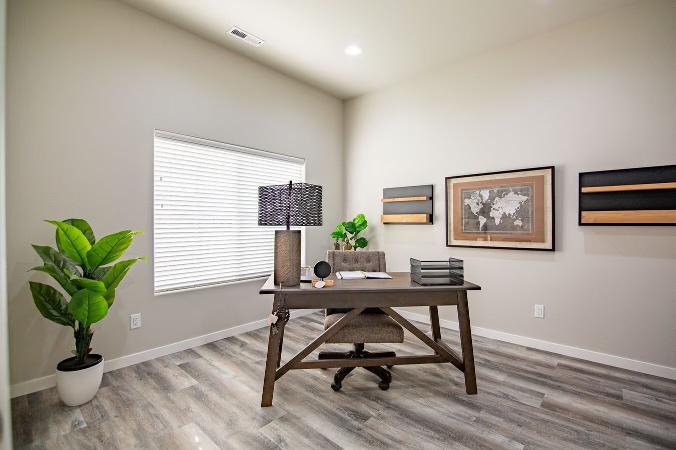 A home office with a dark wood desk, matching chair, houseplant, and framed map on a light gray wall.