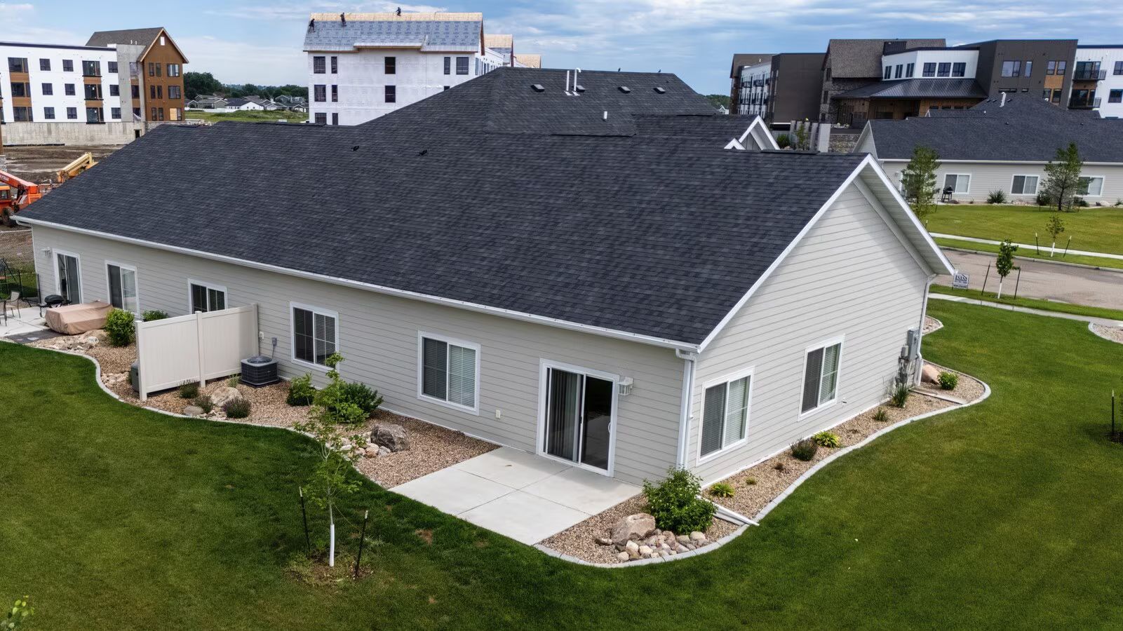 Aerial view of a light-colored, single-story multi-family building with a dark gray roof, surrounded by lawn and landscaping.