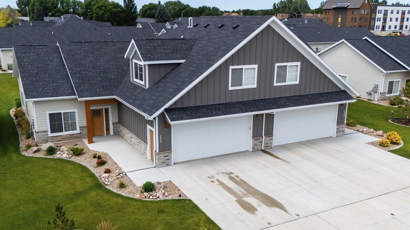 An aerial view of a multi-unit townhouse with a dark shingle roof, gray vertical siding, and a light stone base.