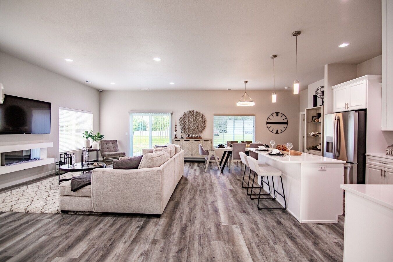 An open-concept living room and kitchen featuring light grey flooring, a white sofa, and a kitchen island with stools.