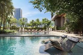 Pool with lounge chairs, trees, and city skyline in background.