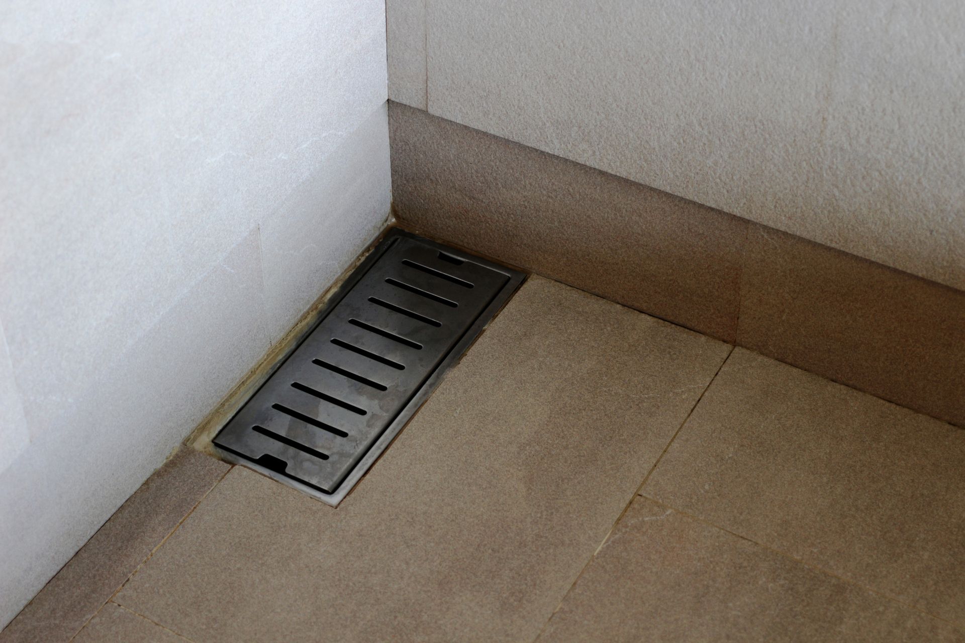 A drain on the floor of a bathroom next to a wall.