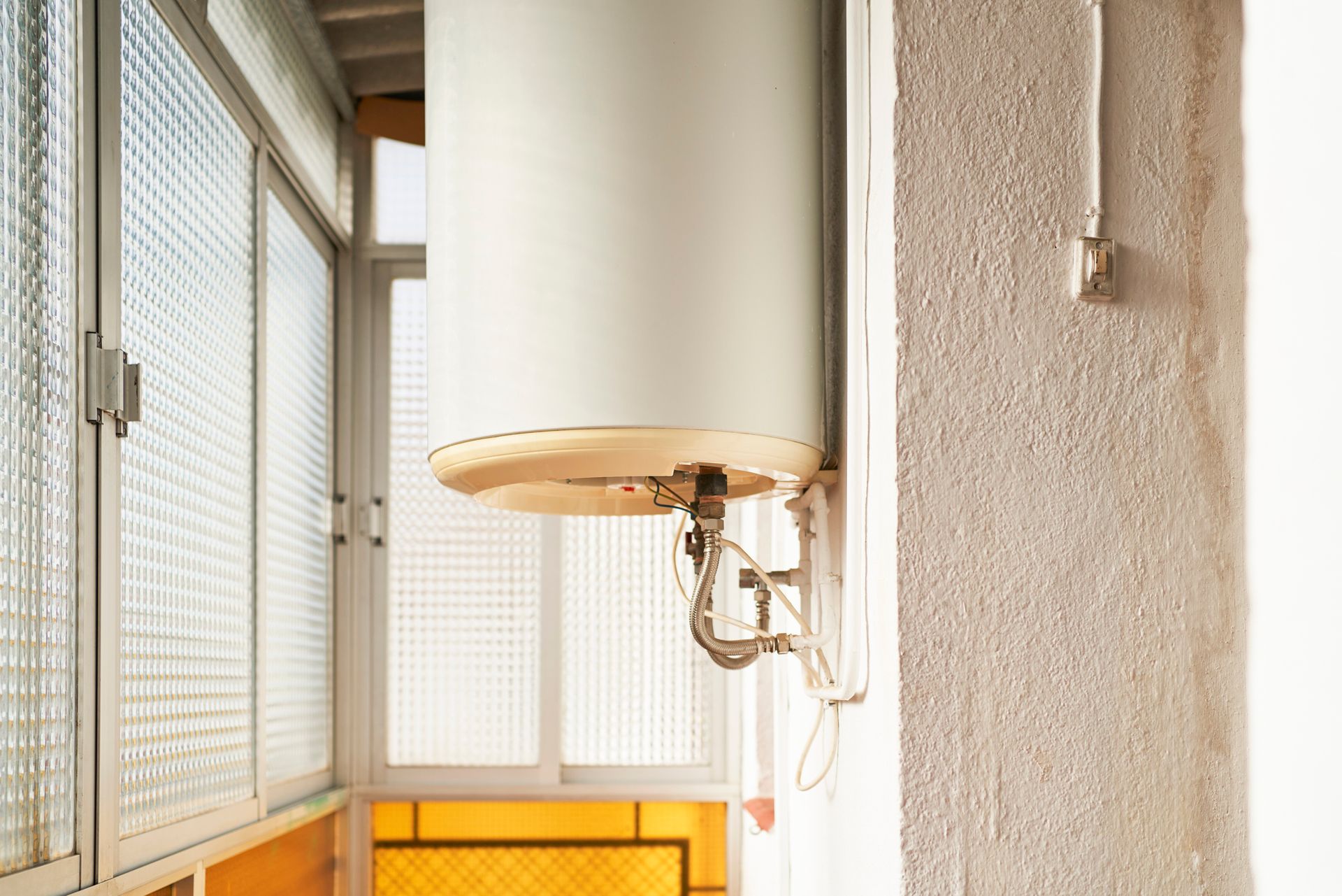 A water heater is hanging on a wall next to a window.