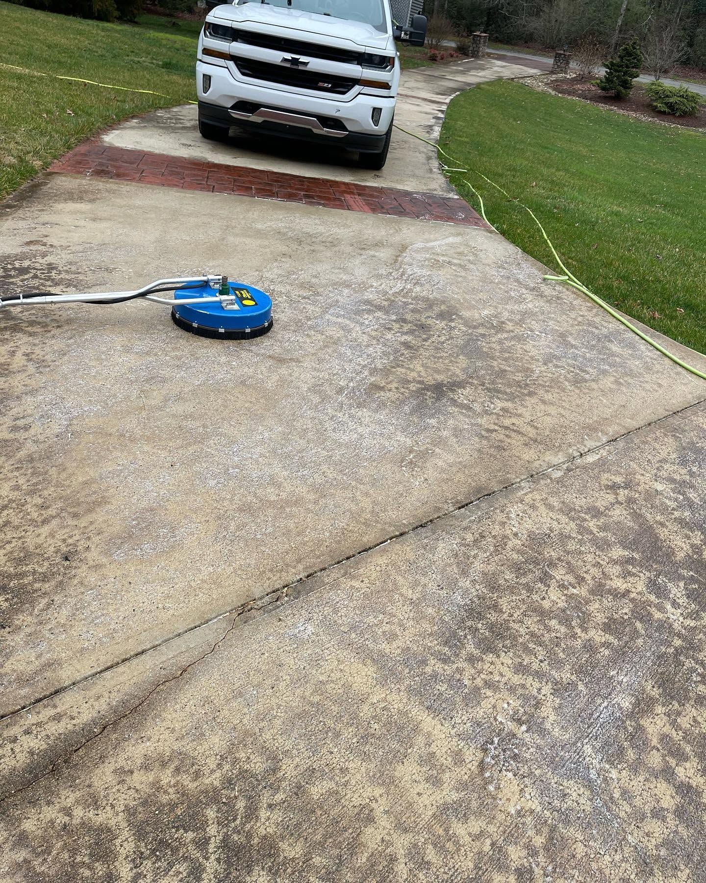 Blue pressure washer cleaning a concrete driveway in front of a white pickup truck.